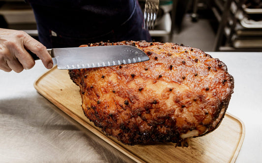 A hand carving a juicy Christmas Ham glazed in Christmas Gin glaze from Four Pillars Gin. 