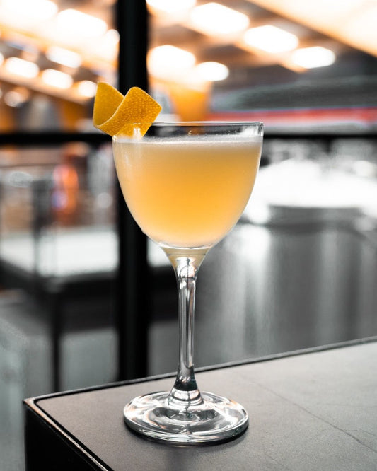 A beautiful, orange Chardonnay Barrel Ages gin cocktail with an orange twist as a garnish. 