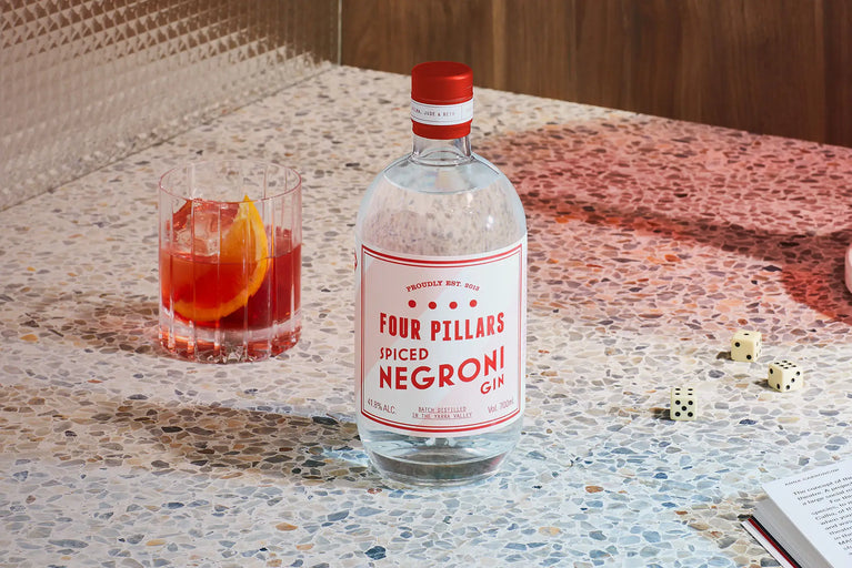 A freshly made negroni cocktail with a wedge of orange, sits beside a bottle of Spiced Negroni Gin from Four Pillars Gin. 