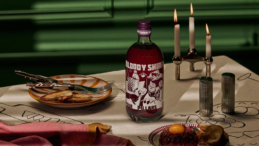 The new Limited Edition Bloody Shiraz Gin from Four Pilars gin with label art by Kris Leombruni, and a candle lit table.