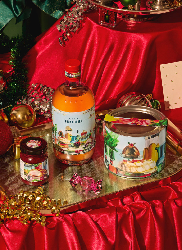 Bottle of Four Pillars gin, canister, and jars on a festive table with red cloth and Christmas decorations.