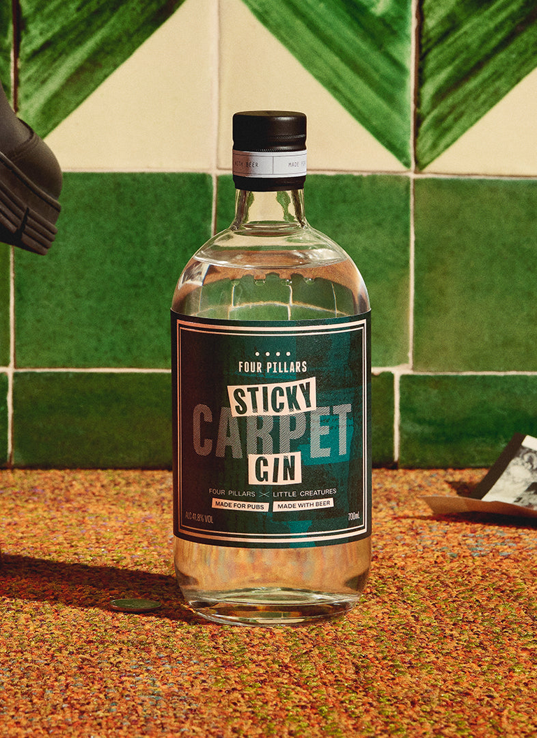  A bottle of Four Pillars gin sits on the sticky carpet of a pub, right next to a chair in front of a green tile wall.