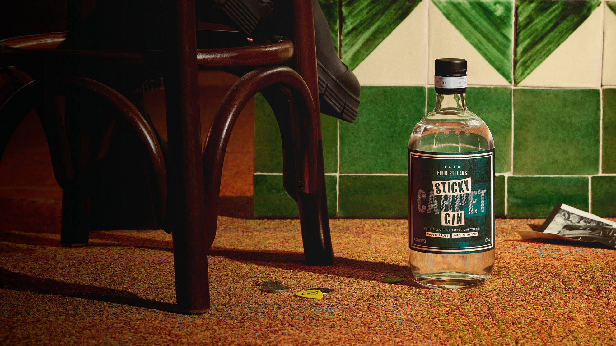 A bottle of Four Pillars gin rests on a sticky pub carpet beside a chair, capturing a cozy night out vibe